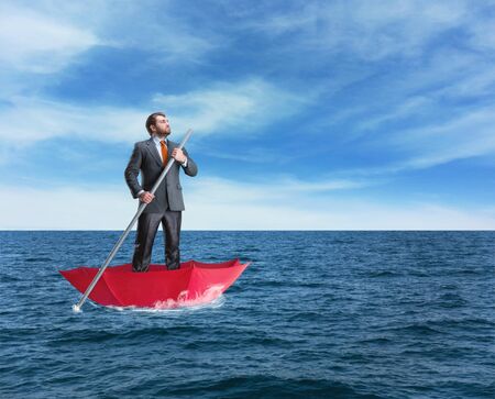 Confident businessman in the umbrella sails in calm seaの写真素材