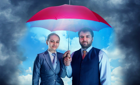 Business couple under umbrella against dark skyの写真素材