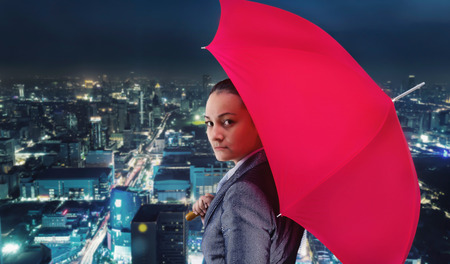 Businesswoman with umbrella against evening cityの写真素材