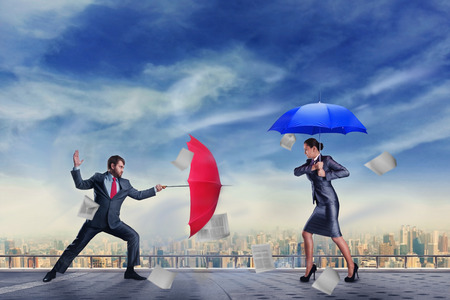 Business people are fighting with umbrellas on the roofの写真素材