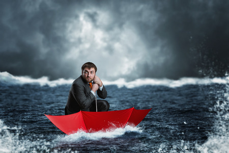 Scared businessman in the umbrella sails in the sea in the nightの写真素材