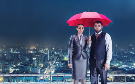 Business couple under umbrella against evening cityの写真素材