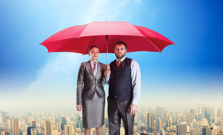 Business couple under umbrella against blue skyの写真素材