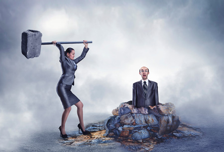 Businesswoman with sledgehammer banging scared worker into the groundの写真素材