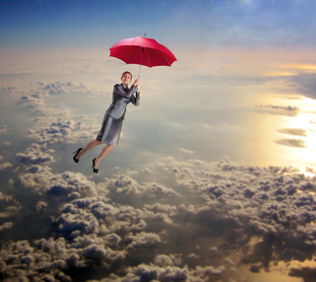 Dreamy woman flying in the sky with red umbrella in her handsの写真素材