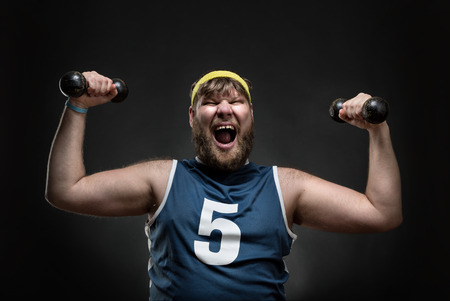 Happy smiling man with dumbbells in his both hands over greyの写真素材
