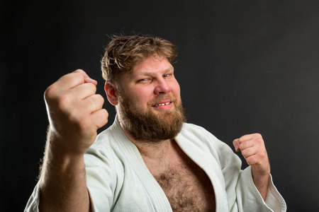 Smiling bearded karate fighter in white kimono shows fistsの写真素材