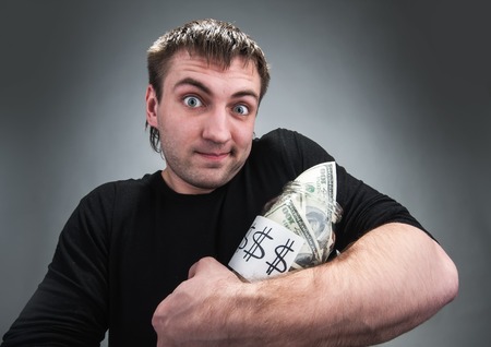 Strange man stands with jar full of dollars over greyの写真素材