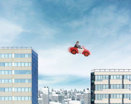 Young businessman driving car jumping between two high buildingsの写真素材