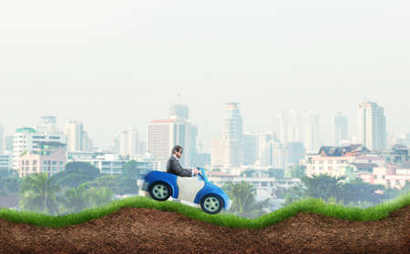 Young businessman driving a toy car on the hillsの写真素材