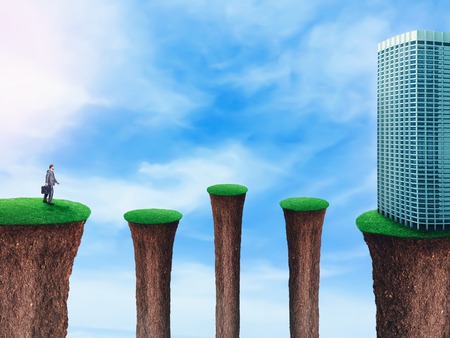 Businessman stepping up on the separated grass hills to the office buildingの写真素材