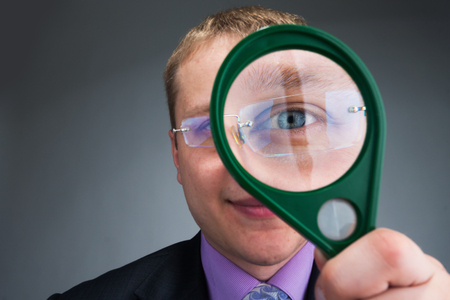 Businessman looks at you through magnifying glassの写真素材
