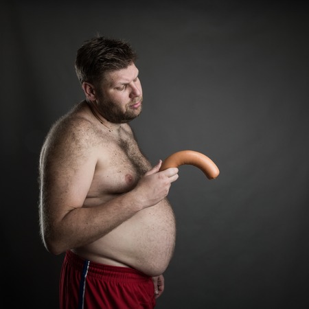 Side view of fat man with a sausage in his hand. Potency problemの写真素材