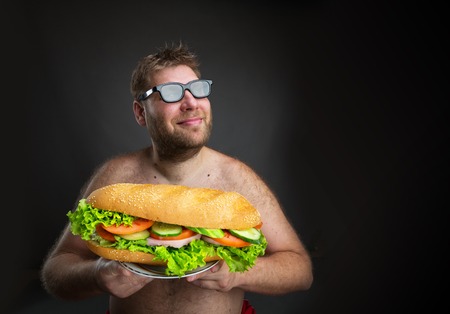 Fat happy man in glasses with sandwich over dark backgroundの写真素材