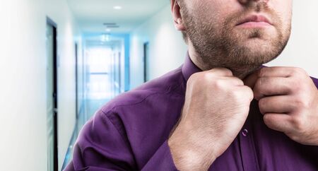 Bearded man buttons his shirt in office corridorの写真素材