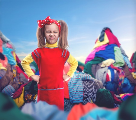 Little girl with her hands on hips stands among heaps of clothesの写真素材