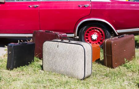 Many old suitcases standing on the grass near a red carの写真素材