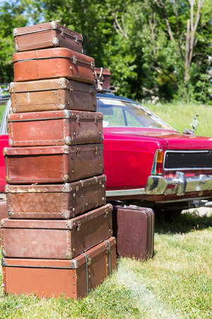 Huge heap of old suitcases standing on the grass near a red carの写真素材
