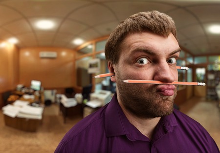 Strange bearded man holds pencil with his nose and lips and one more pencil in his earsの写真素材