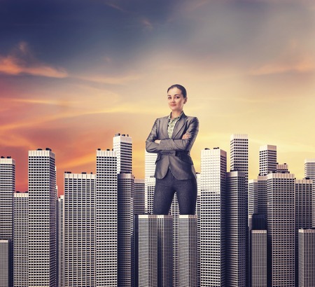 Smiling businesswoman standing among the office scyscrapers  at the sunsetの写真素材