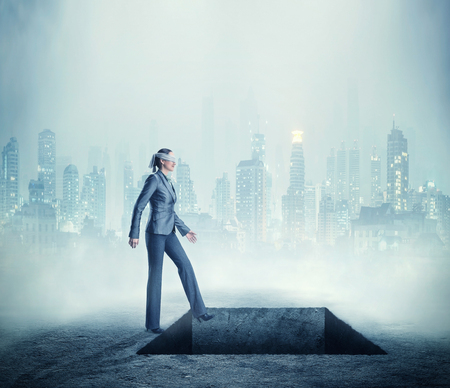 Businesswoman blindfolded standing near a deep pitfall in the townの写真素材