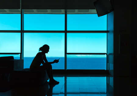 Silhouette of woman with cell phone against the window