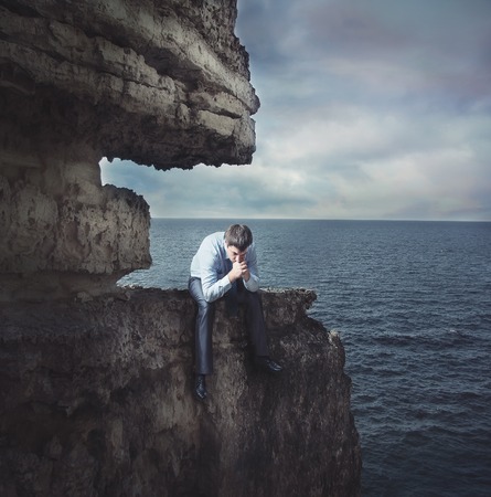 Frustrated businessman sits on edge of the cliff near the seaの写真素材