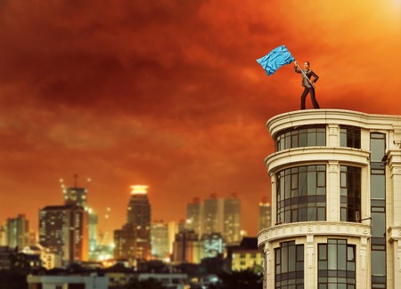 Woman holding a blue flag stands on the top of a high building at nightの写真素材