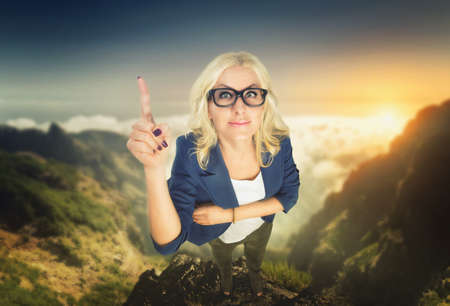 Blonde businesswoman in glasses pointing with her finger stands in the mountainの写真素材