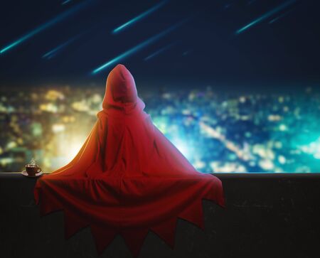 Super hero girl sitting on a high building over the evening cityの写真素材