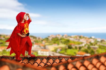 Little girl in a superhero costume standing on the roofの写真素材