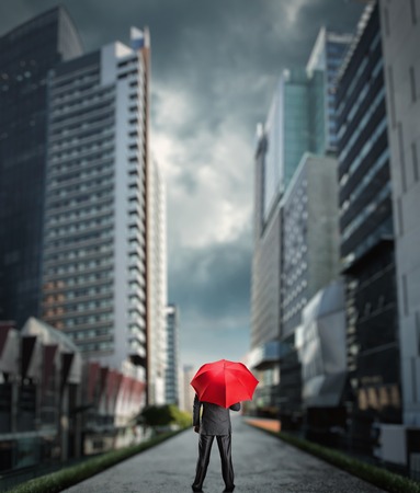 Businessman standing back with a red umbrella in the cityの写真素材