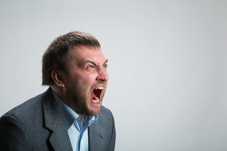 Young angry businessman shouting over greyの写真素材