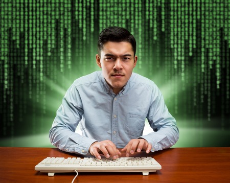 Young programmer working hard sits at the table with keyboard