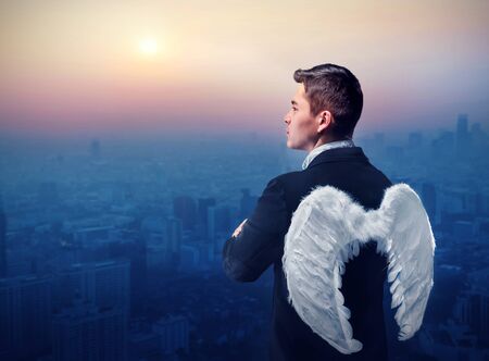 Businessman with angel wings on his back looking at sunrise over cityの写真素材