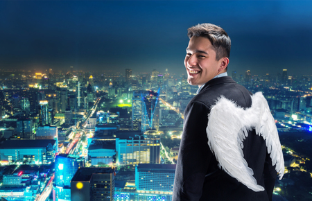 Businessman with angel wings on his back looking at night cityの写真素材