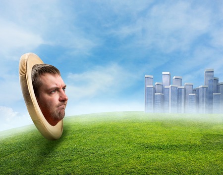 Male face in the coin on the meadow over a town backgroundの写真素材