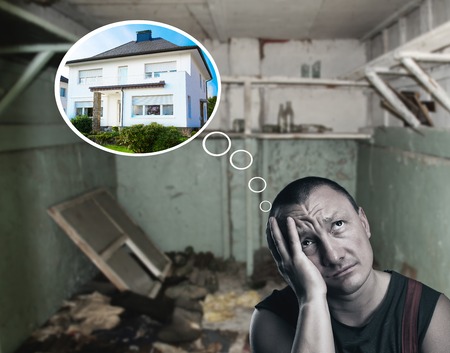 Portrait of sad man sitting in a dirty room dreaming about a new houseの写真素材