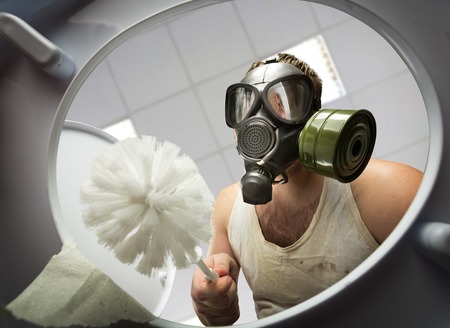 Man in gas mask with brush cleaning the toilet bowlの写真素材