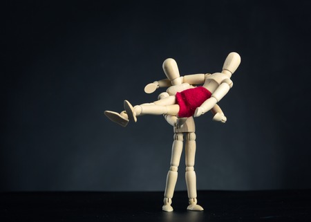 Wooden carved figures, man holding in arms his wife over blackの写真素材