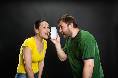 Young couple listening to joke using smartphone over black backgroundの写真素材