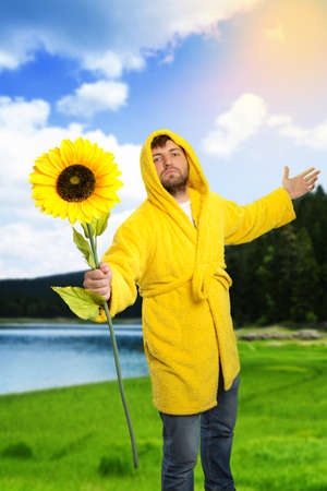 Man in yellow bathrobe holding a sunflower outdoorの写真素材