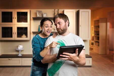 Couple with tablet in the room, woman point at something on the tablet looking over the shoulder