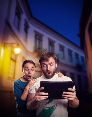 Very excited man and woman playing with tablet on the street in the eveningの写真素材