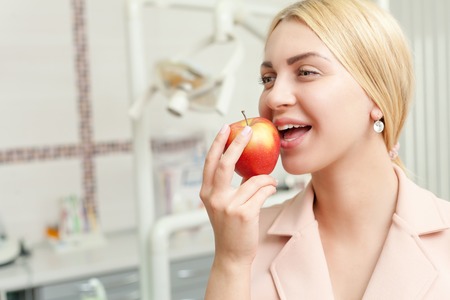 Young woman eating an apple over dentist's office backgroundの写真素材