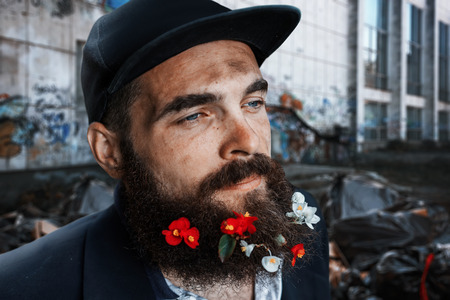 Bearded homeless sitting in flowerbed with flowers in his beardの写真素材