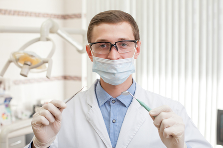 Professional male dentist holding instruments and wearing facemask looks at the cameraの写真素材