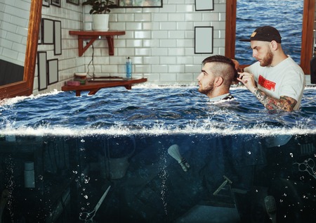 Young man having hair dress in flooded barbershop, barber working with hair clipper