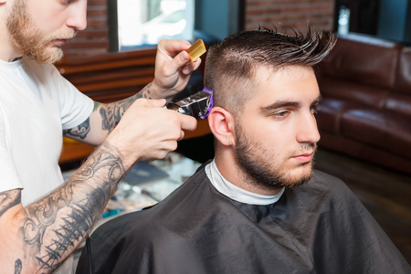 Side view of a young man having hair dress, barber working with hair clipperの写真素材