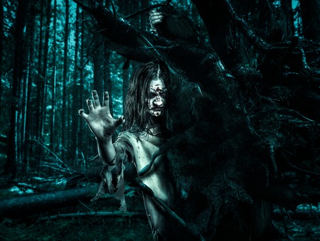 Zombie woman in a dirty dressing gown looks out from behind a tree. Halloween.の写真素材